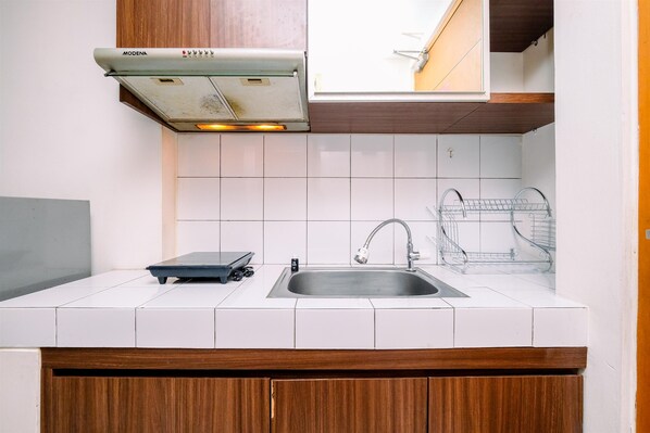 A kitchen with white tiles, a stainless steel sink, a wooden cabinet, and a Modena range hood.