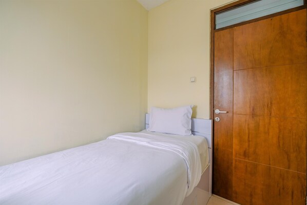 A single bed with white bedding in a room with a wooden door and light yellow walls.