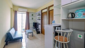 A compact living space with a sofa, a small table, a television, a refrigerator, and a chair. - Cozy And Homey 3Br At Bogor Valley Apartment (Bogor)