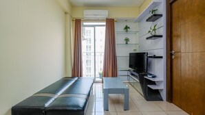 A modern living room with a sofa, a coffee table, a TV, and a shelving unit with plants. - Cozy And Homey 3Br At Bogor Valley Apartment (Bogor)