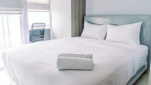 Uma cama bem arrumada com lençóis brancos e uma toalha dobrada, uma cabeceira azul claro e uma cadeira ao fundo.