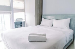 A neatly made bed with white linens and a folded towel, a light blue headboard, and a chair in the background.
