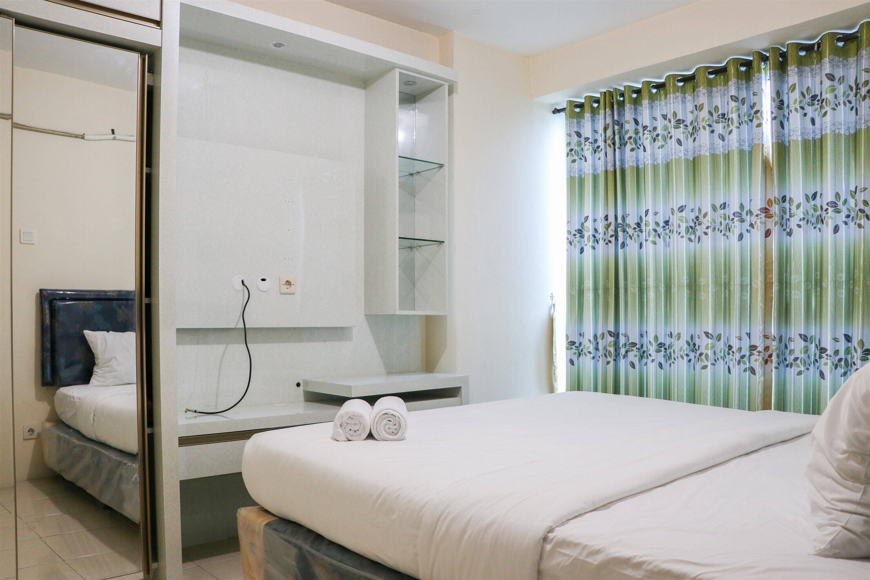 A hotel room with a bed, a built-in wardrobe, a small table, and a shower area.
