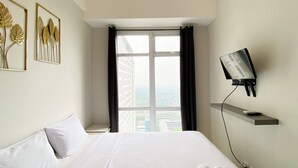 A hotel room with a large bed, a mounted TV, and a window with curtains. - Nice And Elegant 1Br At Vasanta Innopark Apartment (Cikarang)