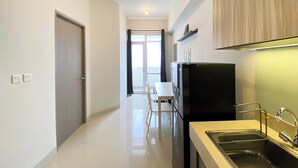 A modern kitchen with a black refrigerator, a sink, and a dining area with a white table and chairs. - Nice And Elegant 1Br At Vasanta Innopark Apartment (Cikarang)