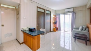Una habitación de hotel moderna con kitchenette, un sofá, una mesa de comedor y un gran ventanal con cortinas.