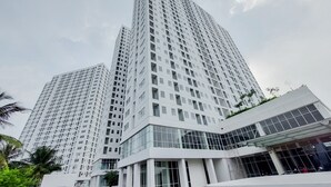 A high-rise building with a modern architectural design, featuring a prominent glass facade and a series of balconies. - Fancy And Nice Studio At Serpong Garden Apartment (Cisauk)