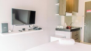A modern hotel room with a flat-screen TV mounted on the wall, a small desk with a kettle, and a bed with a neatly made white towel. - Fancy And Nice Studio At Serpong Garden Apartment (Cisauk)