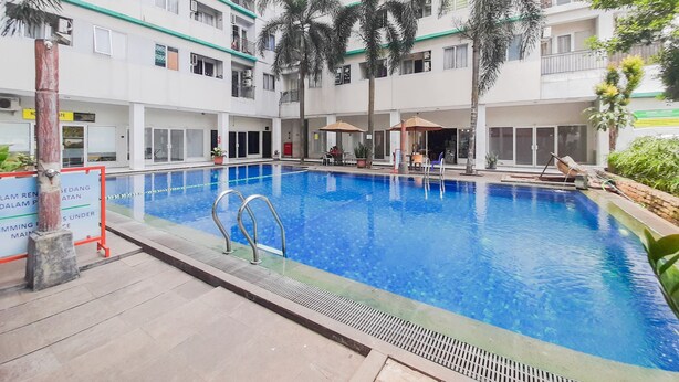 A swimming pool surrounded by a multi-story residential building with balconies and a small outdoor seating area. - Brand New And Super Cozy Studio Room At Sky View Apartment (South Tangerang)