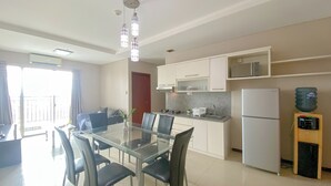 A modern kitchen with white cabinets, a stainless steel refrigerator, and a dining area with a glass table and black chairs. - Spacious And Good 3Br At Thamrin Residence Apartment (Jakarta)