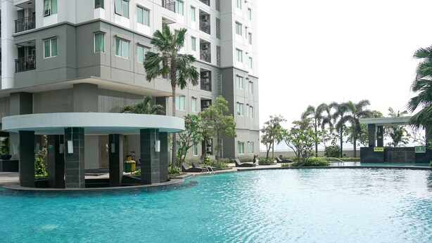A modern hotel with a swimming pool, palm trees, and a covered seating area. - Spacious And Good 3Br At Thamrin Residence Apartment (Jakarta)