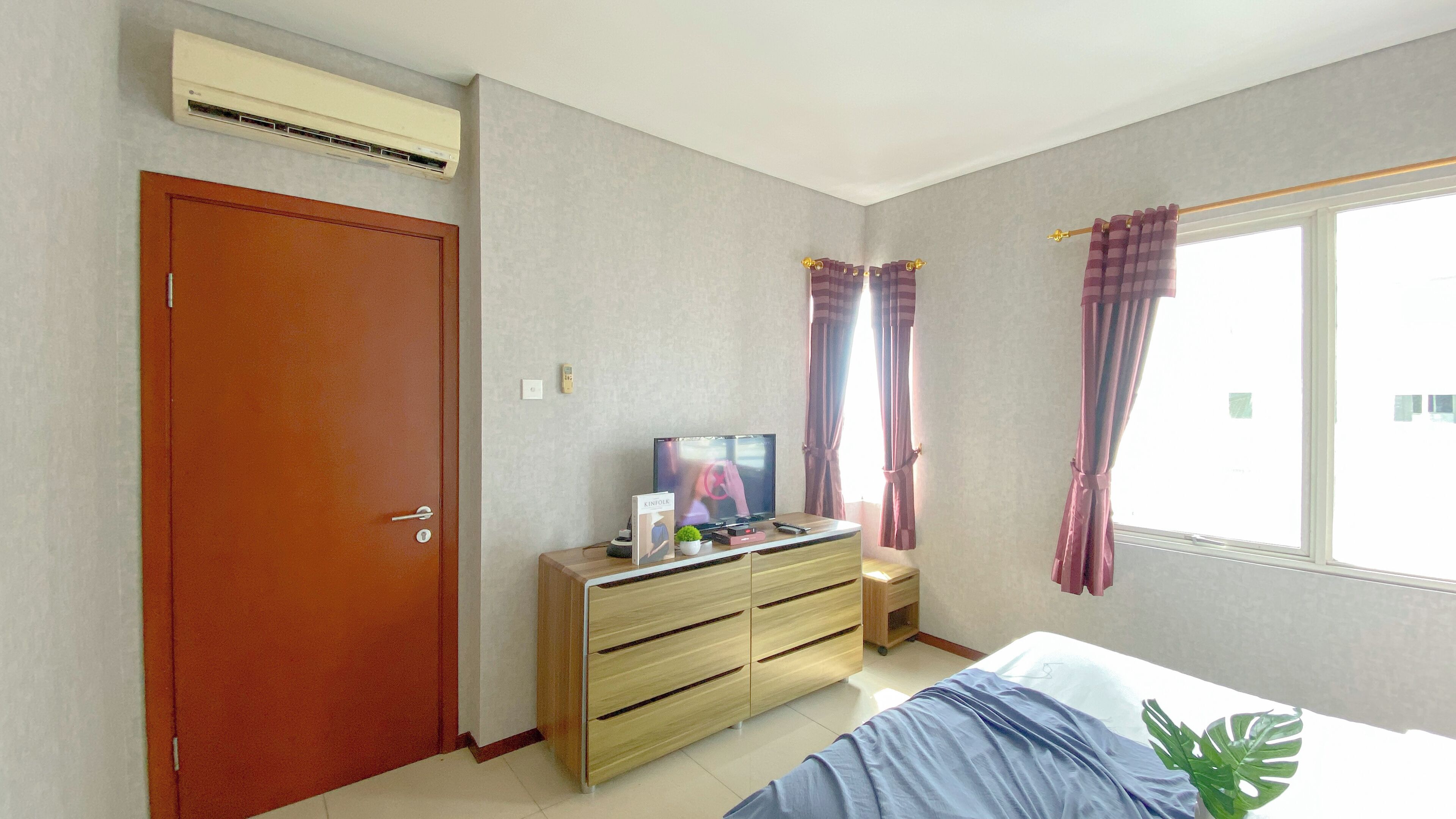A bedroom with a wooden dresser, a television, and a window with curtains.