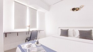 Habitación de hotel con cama, escritorio con silla, ventana y un adorno en la pared.