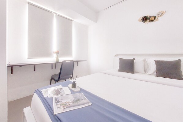 Habitación de hotel con cama, escritorio con silla, ventana y un adorno en la pared.