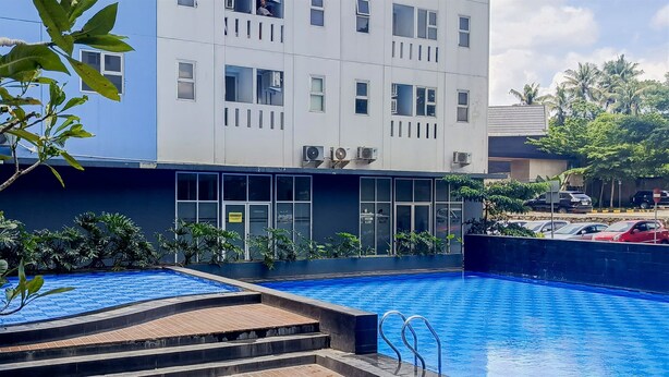 Un edificio moderno con piscina, rodeado de vegetación y un estacionamiento.