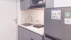 Una cocina con armarios grises, una encimera blanca, un lavamanos de acero inoxidable y un refrigerador Sharp.