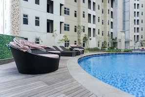 A swimming pool area with lounge chairs and a wooden deck. - Homey 1Br Apartment At Vittoria Residence (Jakarta)
