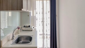 A modern kitchen with a stainless steel sink, a small stove, and a window with sheer curtains. - Warm And Comfortable 1Br Apartment At Vittoria Residence (Jakarta)