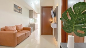 A modern living room with a sofa, a large plant, and a TV mounted on the wall. - Warm And Comfortable 1Br Apartment At Vittoria Residence (Jakarta)