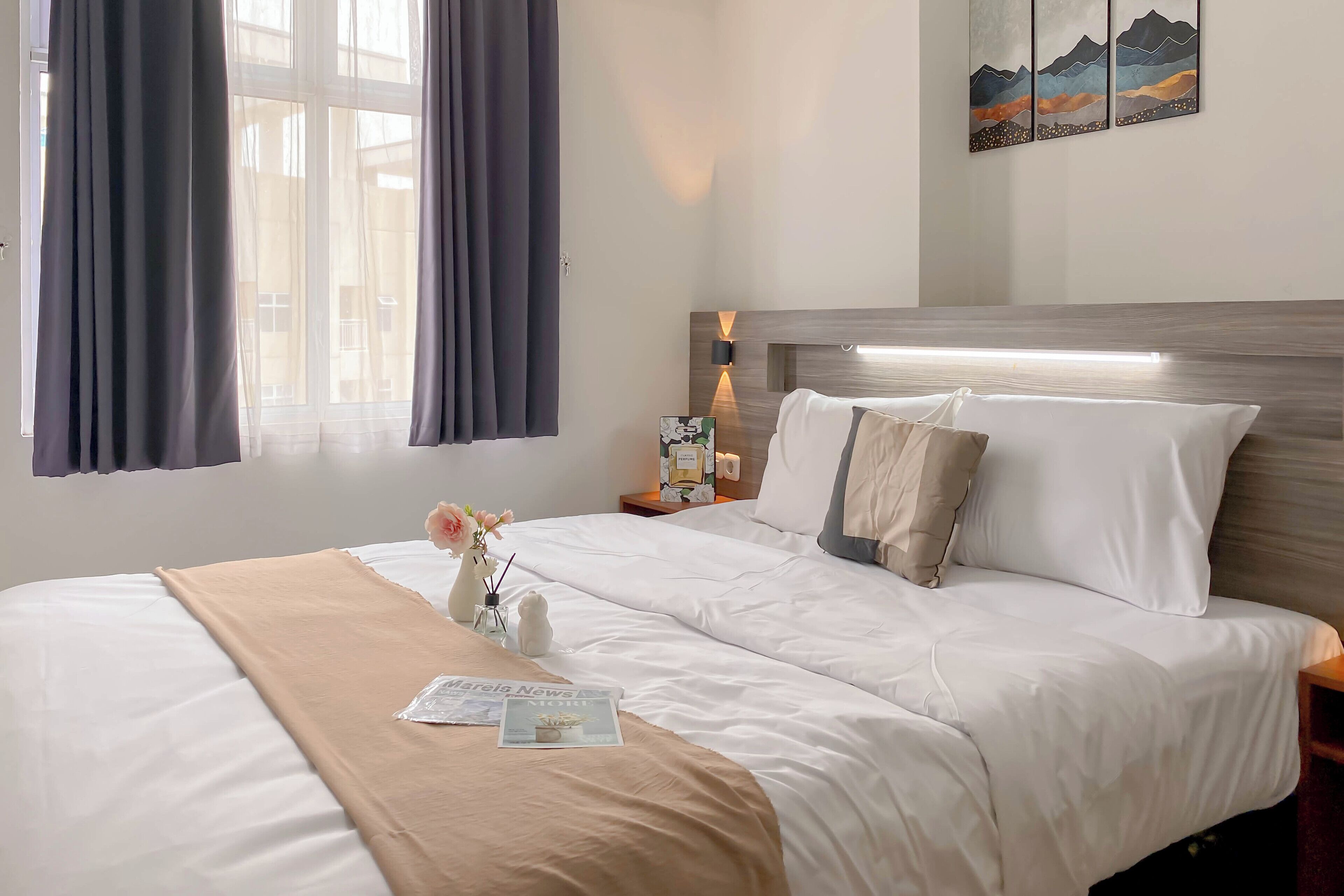 A hotel room with a neatly made bed, a bedside table with a lamp, and a wall-mounted artwork.