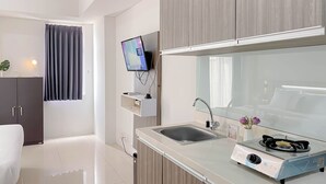 A modern kitchen with a built-in gas stove, a sink, and a flat-screen TV mounted on the wall. - Cozy Studio Apartment At Vittoria Residence (Jakarta)