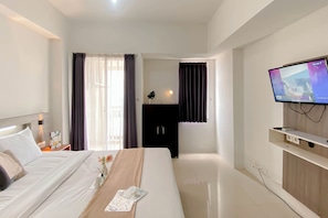 Ein Hotelzimmer mit Bett, Wandfernseher, Schreibtisch mit Lampe und Kleiderschrank.