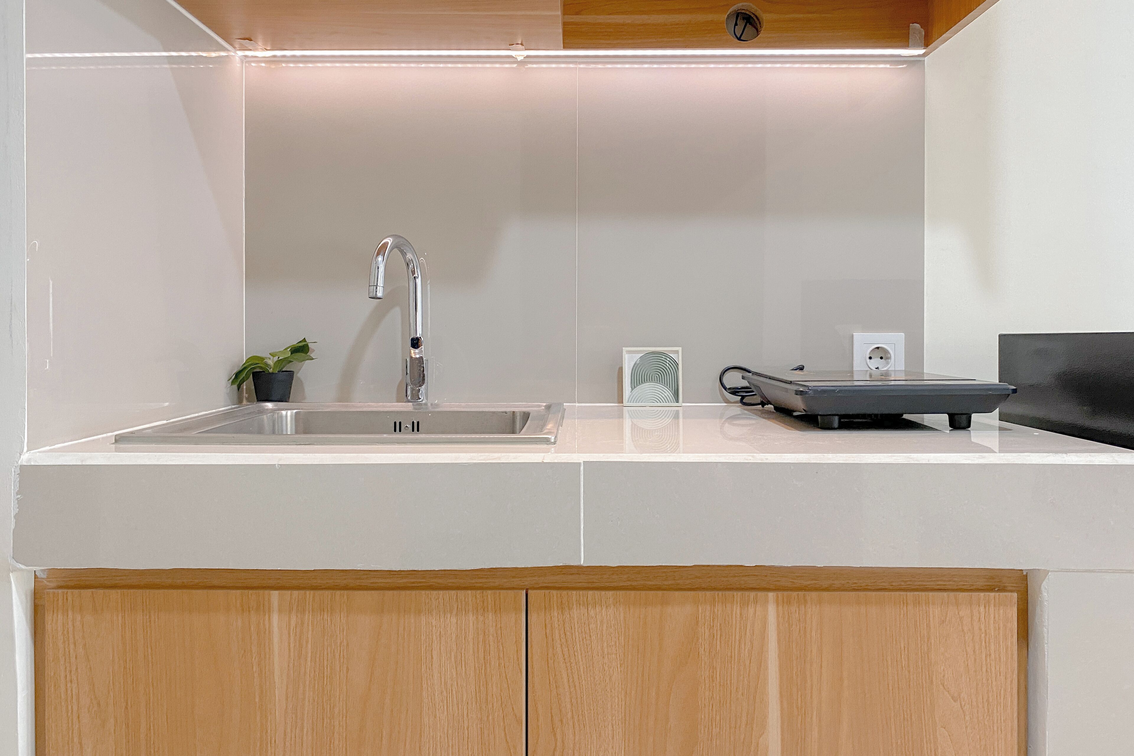 A modern kitchen with a stainless steel sink, a small potted plant, a scale, and a power outlet.