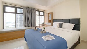Quarto de hotel com cama grande, um assento junto à janela, escrivaninha e vista para a cidade.