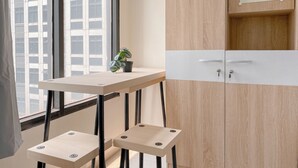 Quarto moderno com armário de madeira, uma mesa pequena com planta em vaso e janela com vista para edifícios.
