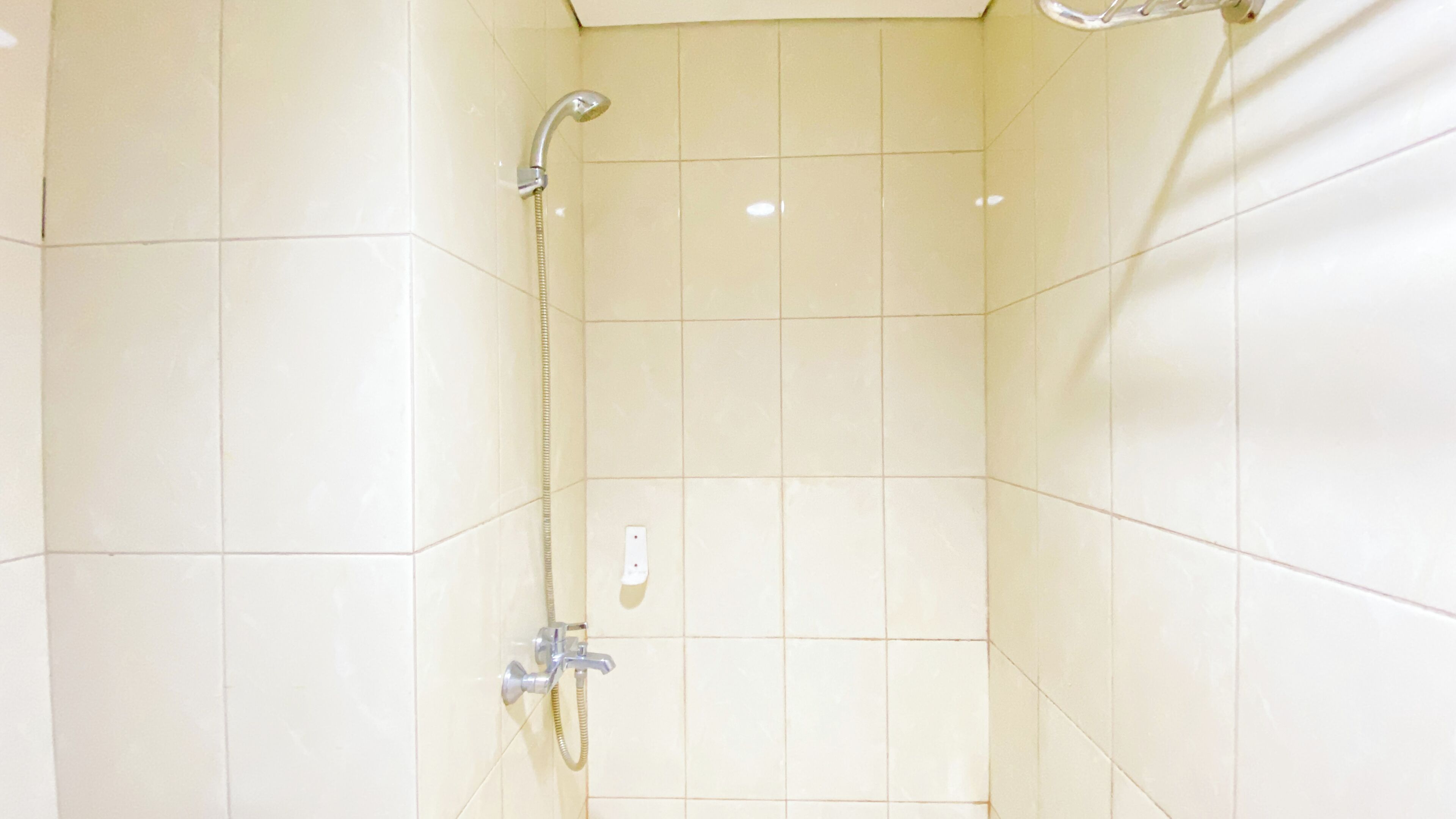 Un petit espace de douche carrelé, équipé d’un pommeau de douche à main et d’un robinet fixé au mur.