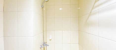 Un petit espace de douche carrelé, équipé d’un pommeau de douche à main et d’un robinet fixé au mur.
