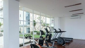 Une salle de sport équipée de matériel d’exercice, dotée de grandes fenêtres et offrant une vue sur des bâtiments et des espaces verts.