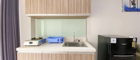 A compact kitchenette with a gas stove, sink, and a black refrigerator.