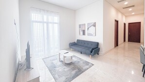 Uma sala de estar moderna com um sofá cinza, uma mesa de centro e uma janela grande com cortinas leves.