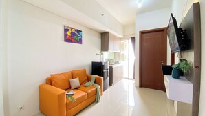 A modern living room with a sofa, a flat-screen TV mounted on a wall, and a kitchen area in the background. - Cozy And Restful 2Br Apartment At Vittoria Residence (Jakarta)