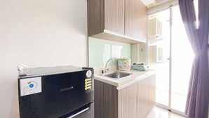 A compact kitchen with a built-in microwave, a sink, and a window with curtains. - Cozy And Restful 2Br Apartment At Vittoria Residence (Jakarta)