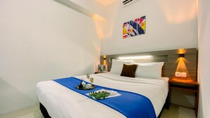 A neatly made bed with a blue accent, a small table with a plant, and a wall-mounted air conditioner. - Spacious And Relaxing 2Br Apartment At Corner Vittoria Residence (Jakarta)