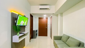 A modern living room with a flat-screen TV, a sofa, and a plant. - Spacious And Relaxing 2Br Apartment At Corner Vittoria Residence (Jakarta)