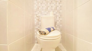 Des toilettes avec une serviette enroulée posée sur le siège, dans une salle de bain dont les murs sont recouverts de carreaux.
