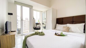 Une chambre d’hôtel avec un lit, un bureau équipé d’un ordinateur, une chaise et un balcon donnant sur des immeubles.