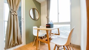 A hotel room with a wooden table, two white chairs, a round mirror, and a view of the city through large windows. - Big 1Br Apartment Tokyo Riverside Pik 2 (Teluknaga)