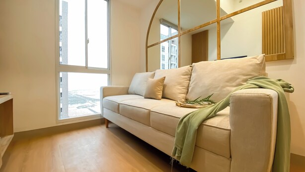 A modern living room with a beige sofa, a green throw blanket, and a small plant on the side. - Big 1Br Apartment Tokyo Riverside Pik 2 (Teluknaga)