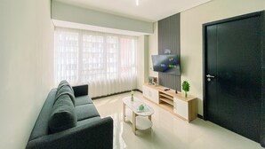 A modern living room with a sofa, a coffee table, a TV mounted on a wall, and a door. - Full Furnished And Homey 3Br Apartment Nifarro Park (Jakarta)