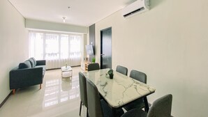 A modern living room with a dining area, featuring a marble table, grey sofas, and a large window with curtains. - Full Furnished And Homey 3Br Apartment Nifarro Park (Jakarta)