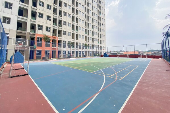 Una cancha de baloncesto al aire libre junto a un edificio de varios pisos con balcones.