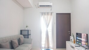 A living room with a sofa, a television, a small table with a vase, and a door. - Good And Comfy 2Br Apartment At Transpark Juanda Bekasi Timur (Bekasi)