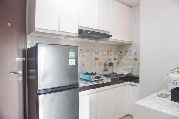 A compact kitchen with white cabinets, a stainless steel refrigerator, a blue portable gas stove, and a white sink.