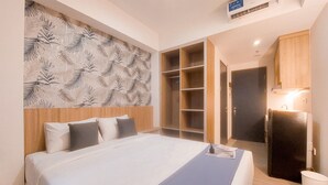 A hotel room with a large bed, a wardrobe with multiple compartments, a built-in shelf unit, and a small trash bin. - Highest Value Studio Room At Collins Boulevard Apartment (Tangerang)