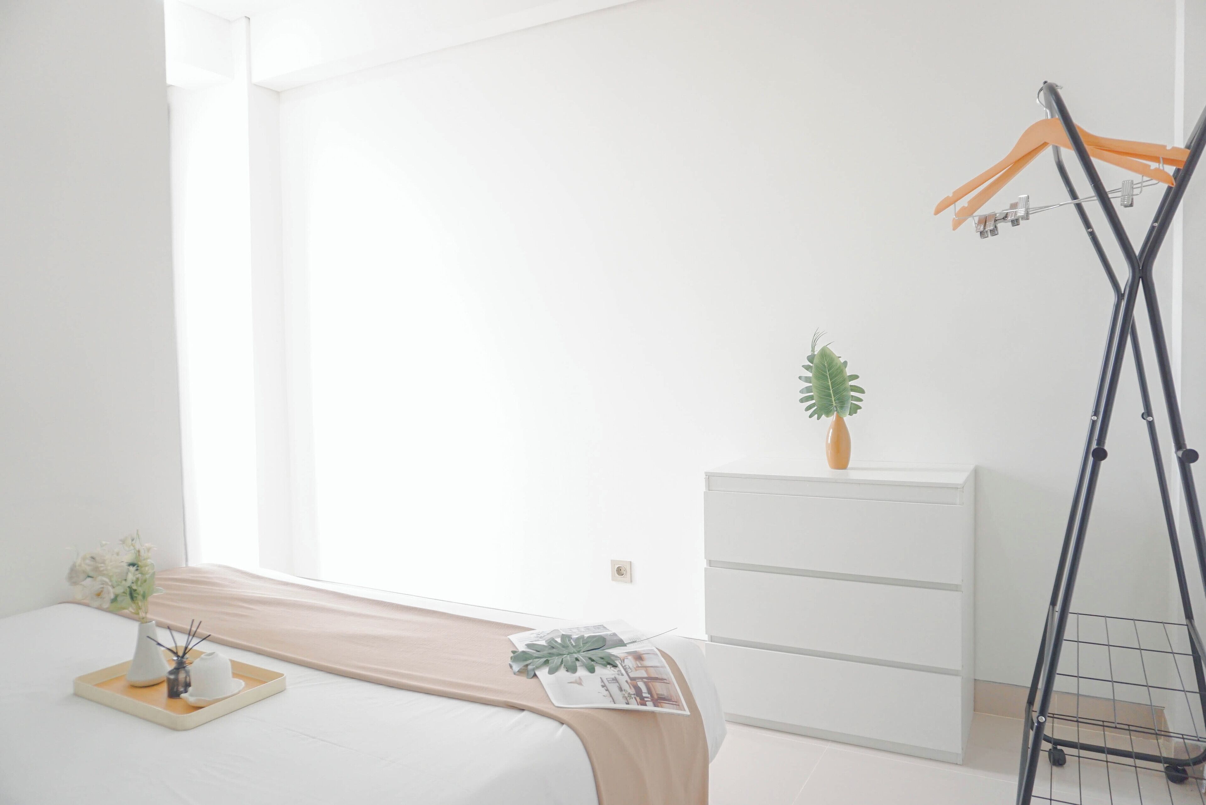 Ein schlicht eingerichtetes Schlafzimmer mit Bett, Kommode, Pflanze und Wäscheständer.