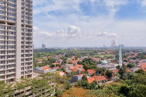A high-rise building with multiple balconies and a view of a cityscape with residential buildings and a mosque. - Cozy Studio Apartment Parkland Avenue (South Tangerang)